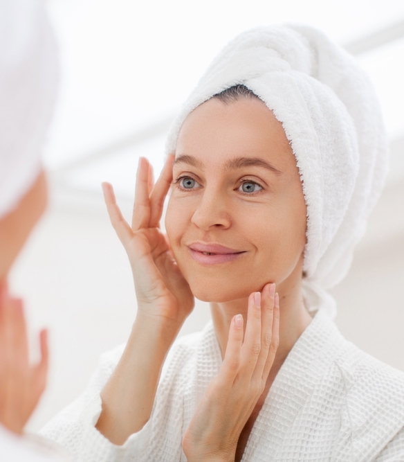 woman in robe and town assessing her face in the mirror after botox